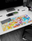 Winking orange-haired anime girl firing a cute water gun on desk pad 36x16 inches, ribbons flying.