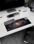 Large 28x12 inch mouse pad featuring a spiral galaxy design with swirling blues, gold tones, and stardust accents.