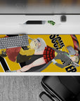Dark-playful anime desk pad 36x16 inches in mustard yellow, crisp grays, red plaid, and neon scythe energy.