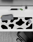Whimsical 32x12 mouse pad featuring cow print-inspired design with black and white spots for a fun, creative workspace aesthetic
