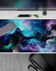 Mysterious 40x20 desk pad showcases cosmic dance with vibrant hues for an immersive workspace vibe