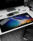 Star-filled sky over pine silhouettes desk pad 40x20 inches, deep blue tones with low amber horizon.
