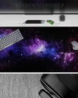 Galaxy-inspired desk pad 40x20 inches with black nebula clouds, violet haze, and blue stardust design.