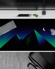40x20 inches desk pad with a futuristic, neon-inspired design of geometric pyramids illuminated by green and blue under a crescent moon.