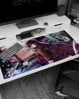 Anime girl leaning on bike in long brown coat and red tie desk pad 40x20 inches, city backdrop.
