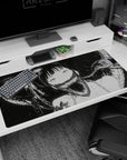 Pale wide-eyed anime girl grinning as black shadows curl behind her on a 40x20 inches desk pad.