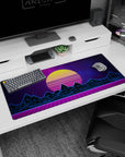 Artistic 36x16 inches desk pad featuring synthwave design, with a glowing yellow sunset, neon blue mountains, and a purple grid for nostalgic energy.
