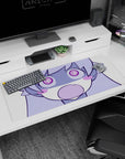Chibi anime girl with puffy cheeks and wide spiral eyes staring at you on desk pad, 36x16 inches.