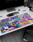 Four laughing anime girls amid bright paint bursts on extra large desk pad 40x20 inches, smooth glide.