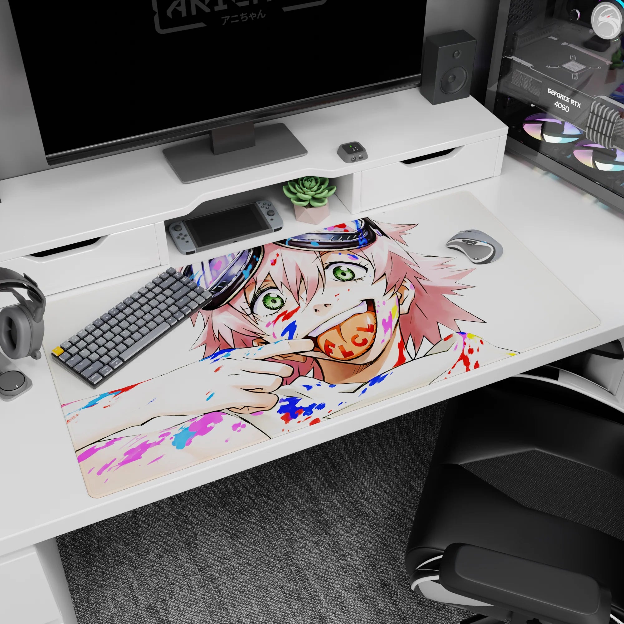 Pink-haired anime girl with chunky goggles and cheeky grin on a 40x20 inches desk pad, paint splashes behind.