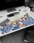 Schoolgirls huddle on anime desk pad 40x20 inches, one winks with peace sign, another shyly covers smile.