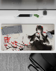 Moody ink-wash gray anime desk mat 32x16 inches with raven-haired girl and crimson blossoms.