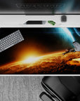 Moody 40x20 inches desk pad in inky blacks and molten orange-gold glow, cozy sunrise-in-orbit vibe.