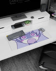 Chibi anime girl with puffy cheeks and wide spiral eyes staring at you on desk pad, 28x12 inches.