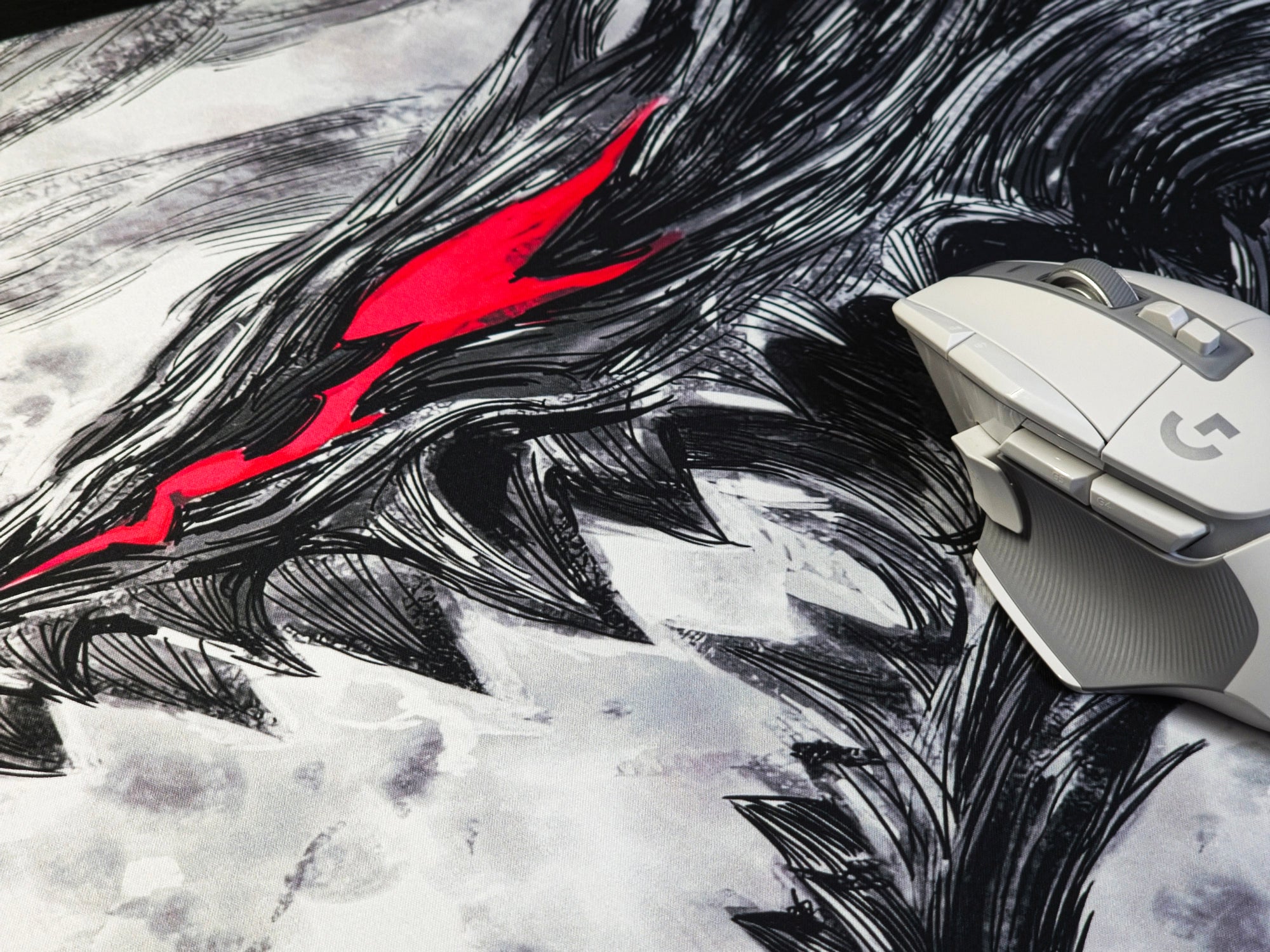 Close-up of a white gaming mouse on an anime-inspired desk mat featuring a black ink-style creature with glowing red eyes.