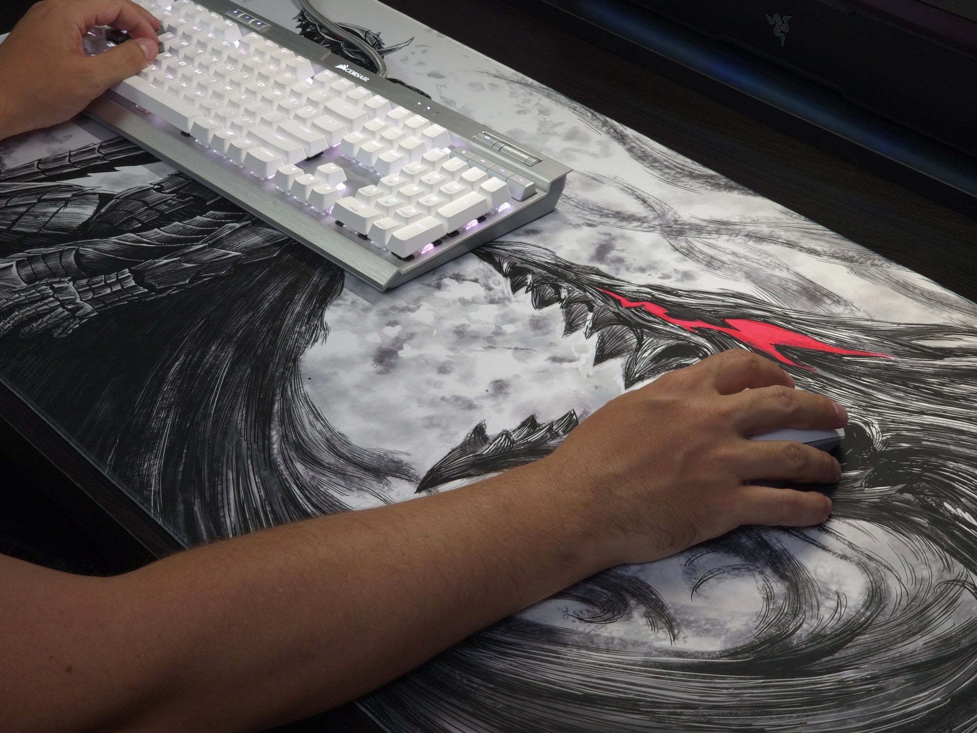 A large desk mat featuring a black and white anime-style illustration of a female character with red eyes, shown with a keyboard and mouse in use on a desk with a person's hands visible.